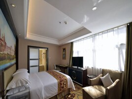 Quarto de hotel com cama, escrivaninha, televisão, cadeira e um quadro na parede.