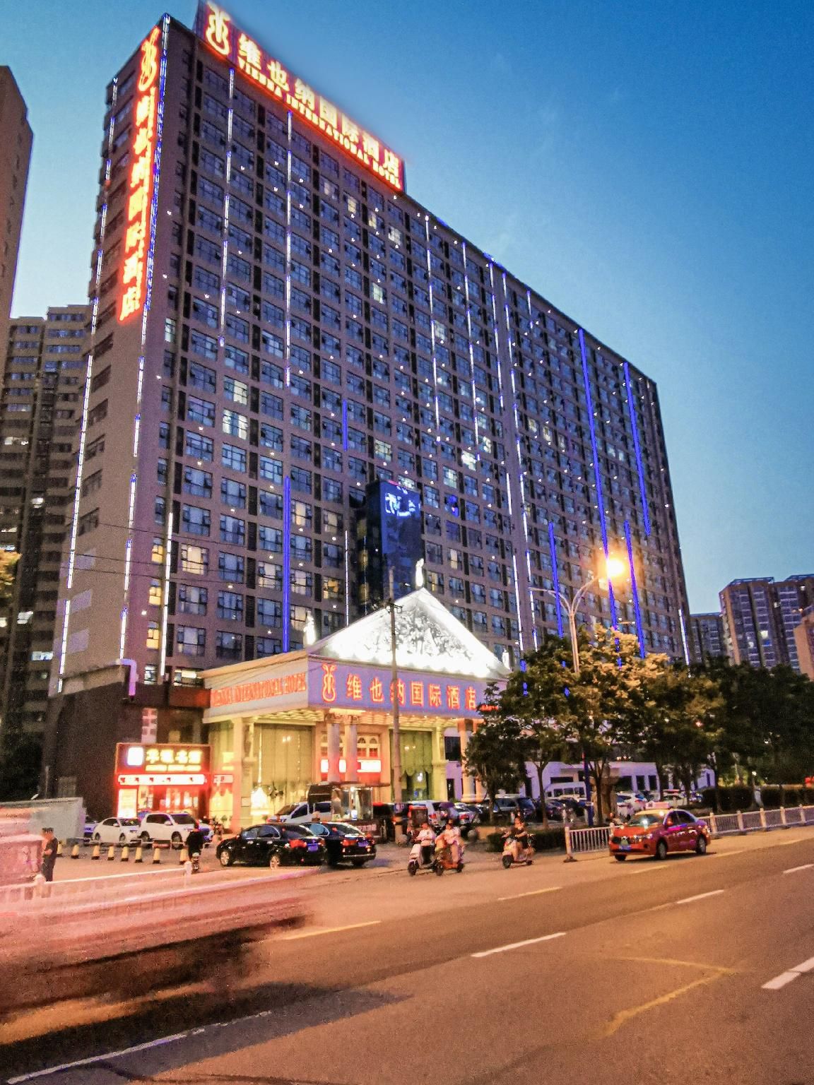 Un hotel de varios pisos con un letrero llamativo en la parte superior, una entrada amplia con un toldo y una calle concurrida enfrente.