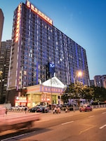 Un hotel de varios pisos con un letrero llamativo en la parte superior, una entrada amplia con un toldo y una calle concurrida enfrente.