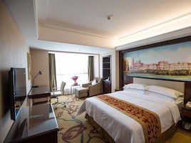 Una habitación de hotel con cama, escritorio, silla, televisión y un cuadro en la pared.