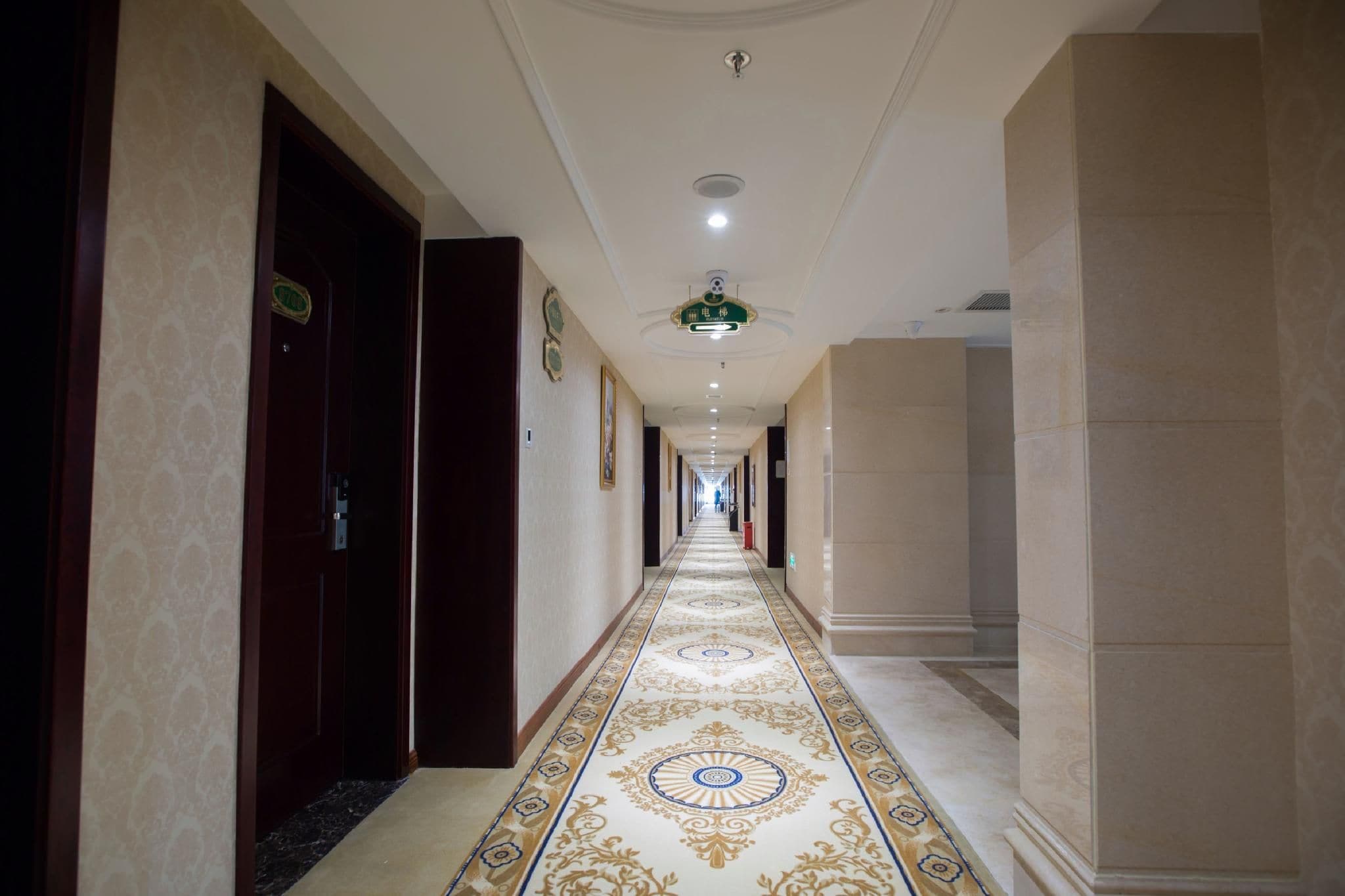 A hotel corridor with a patterned floor, doors on both sides, and a ceiling light fixture.