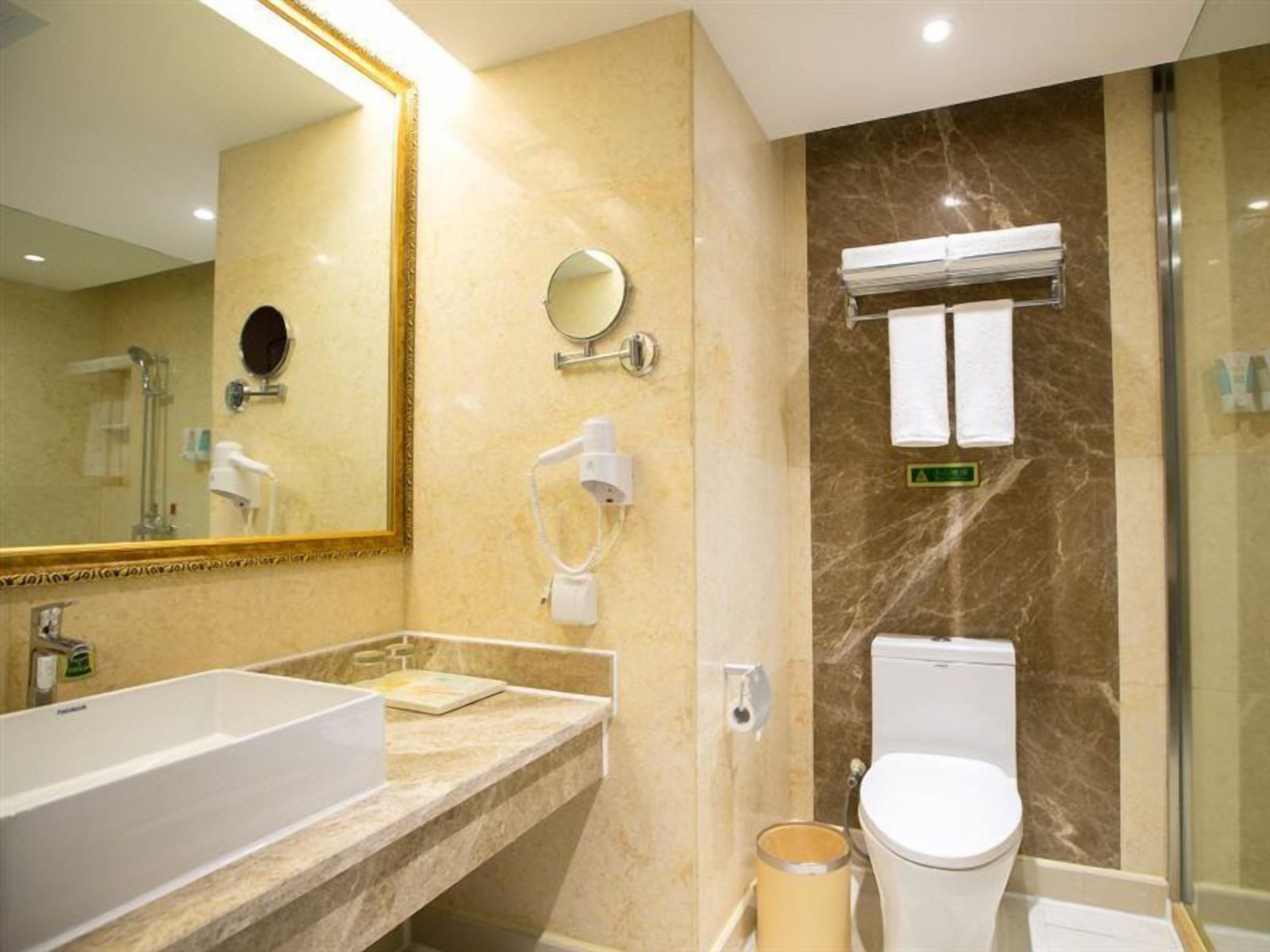 A modern bathroom with a large mirror, a sink, a toilet, and a shower area.
