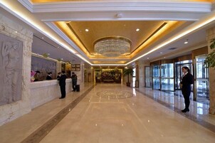 Un vestíbulo de hotel con mostrador de recepción, una araña y suelo de mármol.