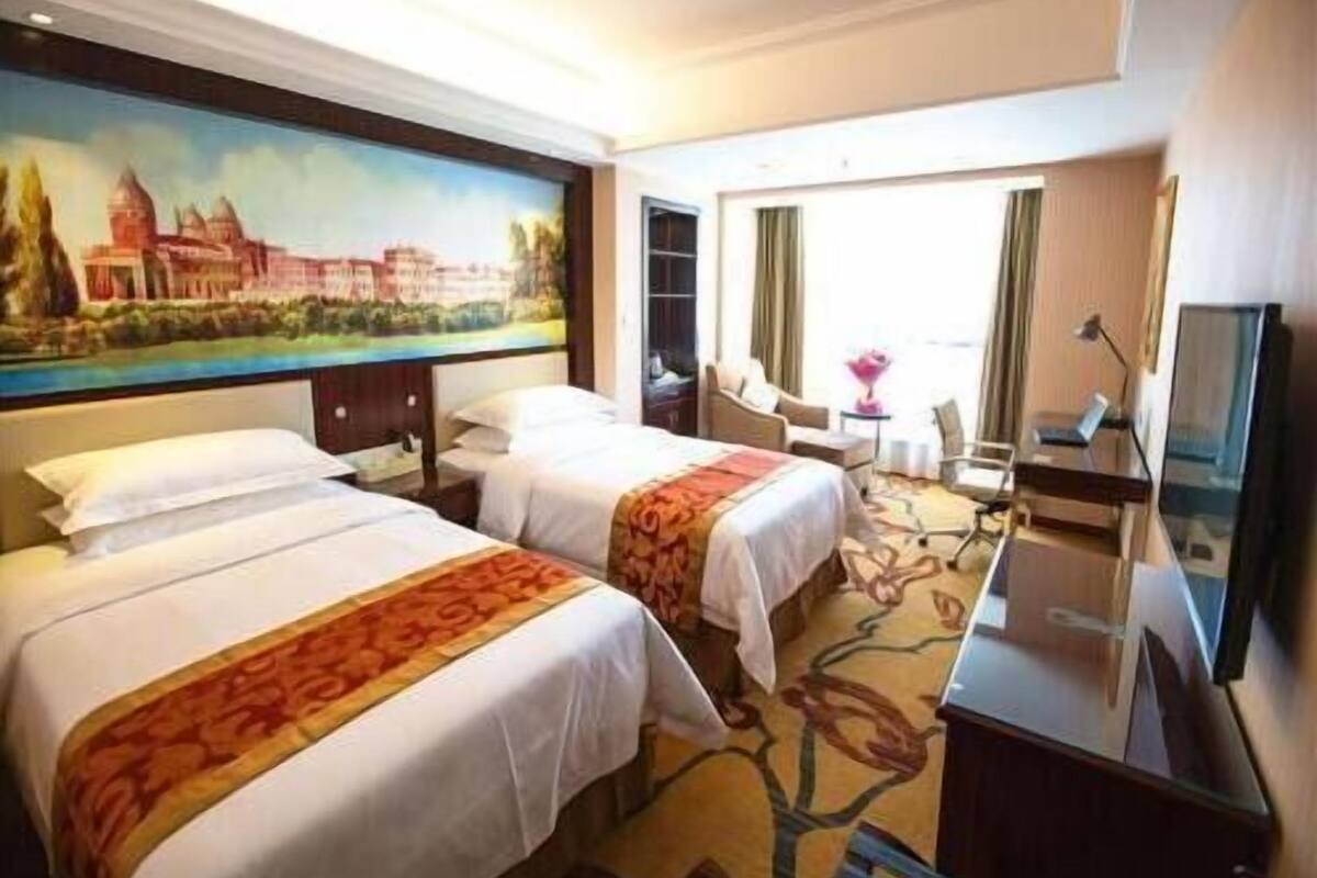 Habitación de hotel con dos camas, un escritorio, una silla, un televisor y un cuadro en la pared.