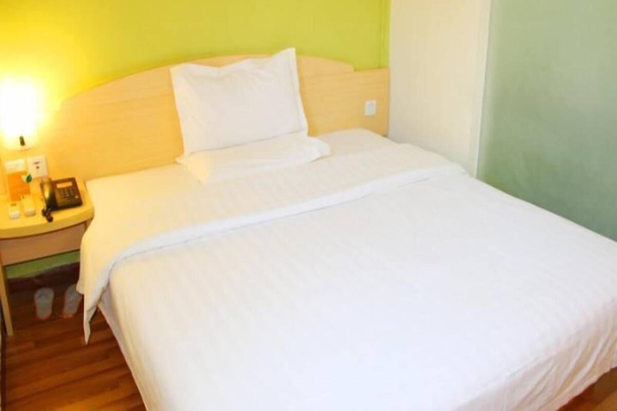 A hotel room with a bed, a nightstand, and a wall-mounted lamp.