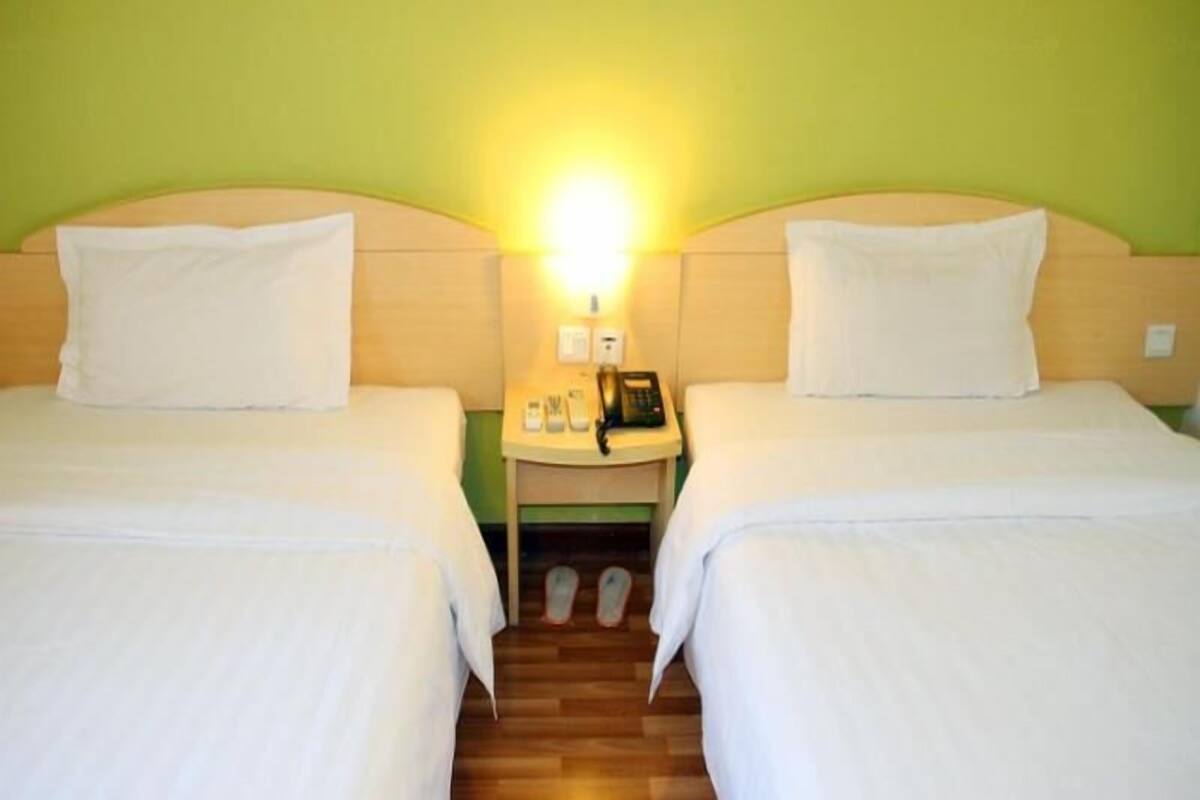 A double room with two beds, a nightstand with a phone, and a wall-mounted light.