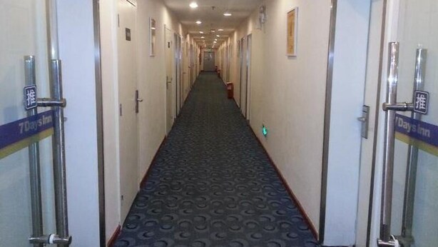 A hotel corridor with doors on both sides, a patterned carpet, and a sign indicating the hotel name.