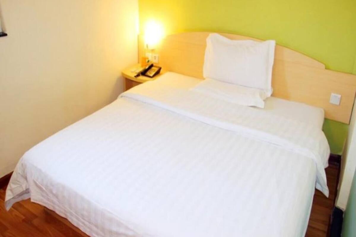 A clean, well-lit hotel room with a bed, bedside table, and a lamp.