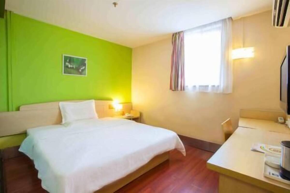 A hotel room with a bed, bedside table, lamp, and a window with curtains.