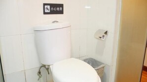 A small, white toilet with a green floor, a trash bin, and a toilet paper dispenser on the wall.