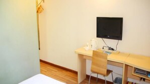 A room with a bed, a desk with a chair, a television, and a trash bin.