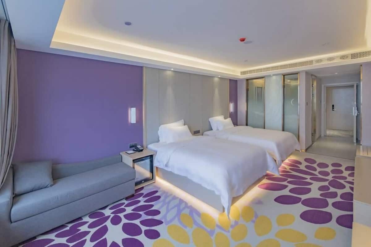 A hotel room with a bed, a sofa, a nightstand, and a mirror.