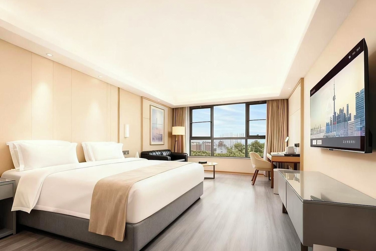 A modern hotel room with a large bed, a desk, a chair, and a television mounted on the wall.