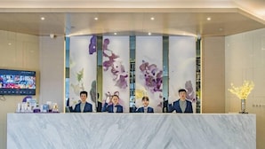 Ein Empfangstresen mit Marmorplatte, einem Fernsehbildschirm und einer dekorativen Wandverkleidung mit abstrakten floralen Motiven.