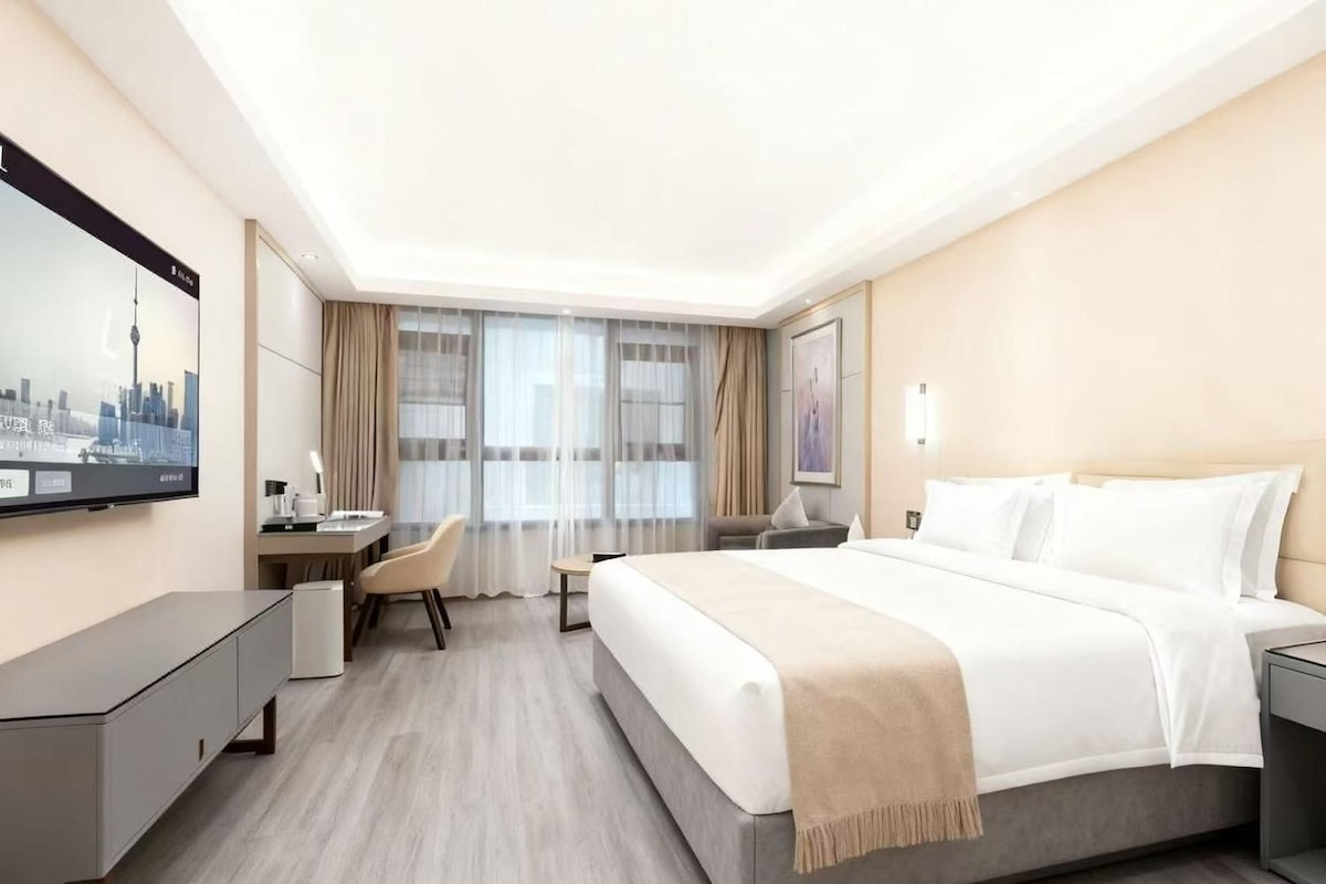 A hotel room with a bed, bedside tables, a desk, a chair, and a television mounted on the wall.