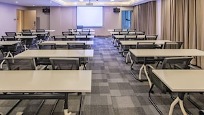 Ein Konferenzraum mit mehreren Tischen und St ühlen, einer Projektionsleinwand und einem großen Fenster mit Vorhängen.