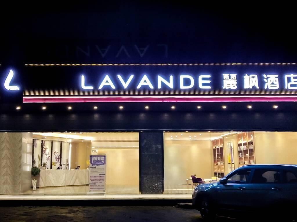 Entrada de hotel con un letrero de neón, un mostrador de recepción y un coche estacionado afuera.