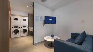 A hotel room with a washing machine, a small table with a vase, and a blue couch. - Holiday Inn Express Qiliping by IHG (Leshan)
