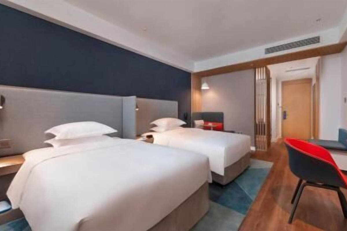 A hotel room with two beds, a desk, a chair, and a TV.