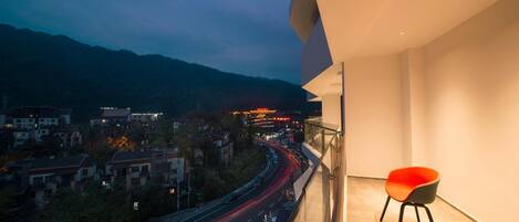 Un balcón con vistas a un paisaje urbano, una silla y una calle con estelas de luz.