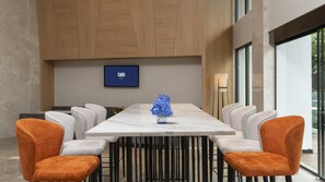 A modern conference room with a marble table, white and orange chairs, and a blue flower centerpiece.