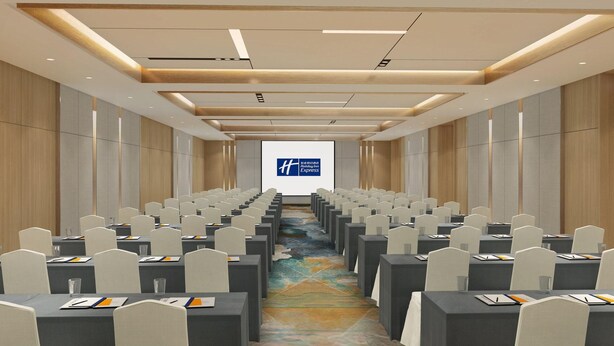 A conference room with rows of tables and chairs, a large screen at the front, and a wooden ceiling design. - Holiday Inn Express Qiliping by IHG (Leshan)