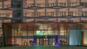 A multi-story hotel with a glass facade, a prominent entrance with a blue-lit canopy, and a sign for 'Holiday Inn Express.' - Holiday Inn Express Qiliping by IHG (Leshan)