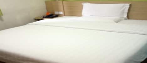 A neatly made bed with white linens in a room with a green wall and wooden flooring.