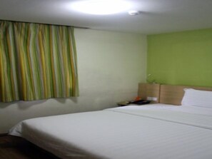 A hotel room with a bed, a headboard, a window with curtains, and a green wall. - 7days Inn Hotel (Bijie)