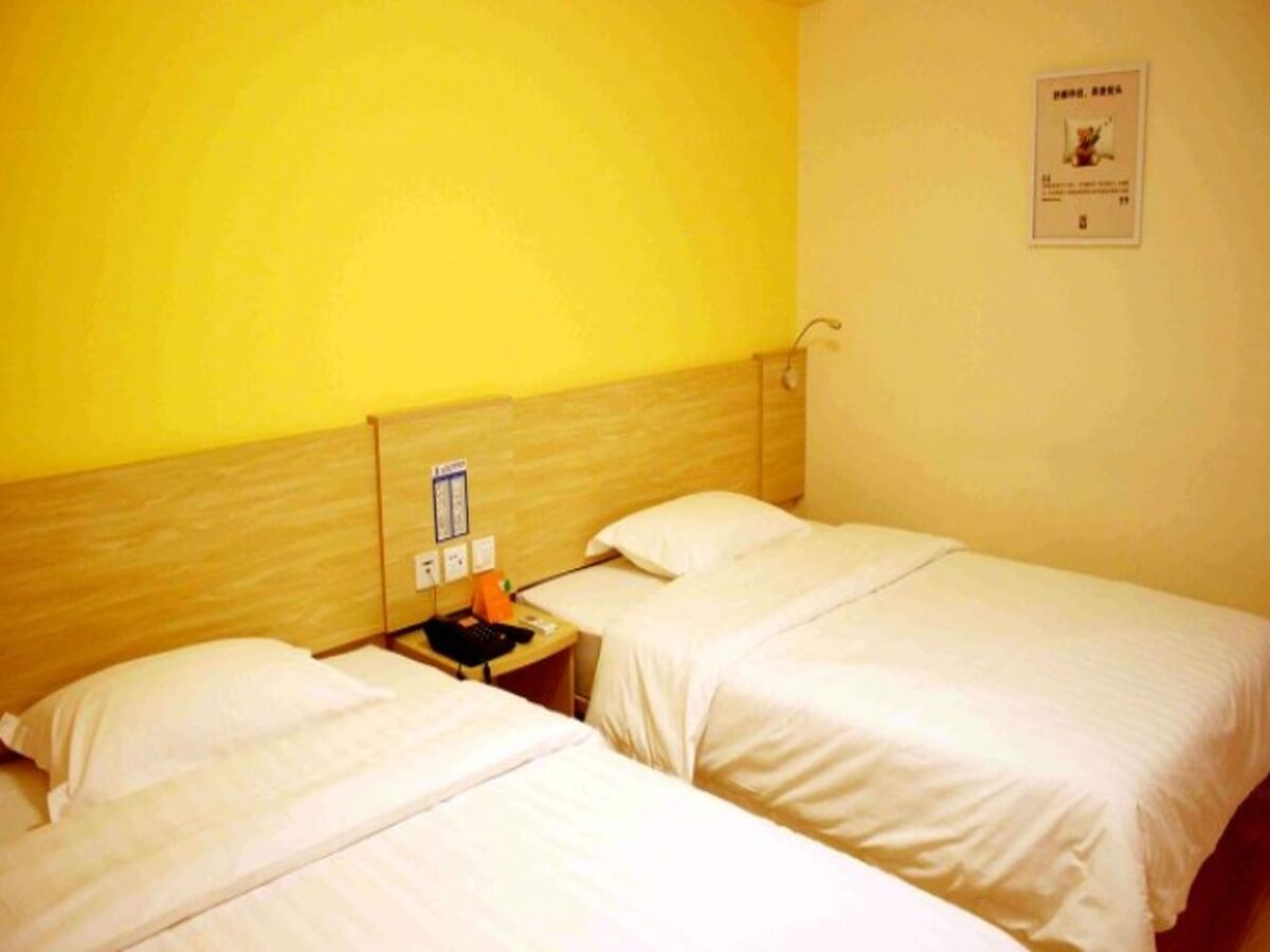 A hotel room with two single beds, a wooden headboard, a small table with a phone and a lamp, and a wall-mounted sign.