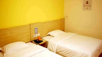 A hotel room with two single beds, a wooden headboard, a small table with a phone and a lamp, and a wall-mounted sign.