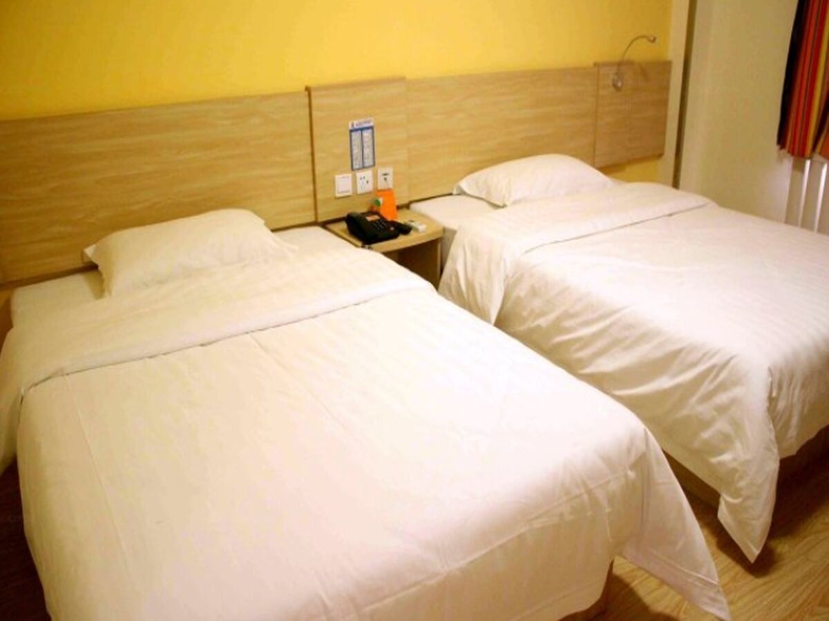 Two single beds with wooden headboards, a nightstand with a phone and a small table, and a wall-mounted light switch.