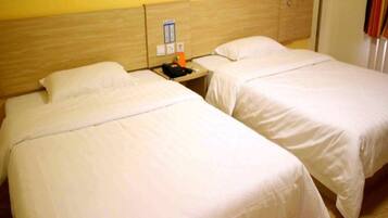 Two single beds with wooden headboards, a nightstand with a phone and a small table, and a wall-mounted light switch.