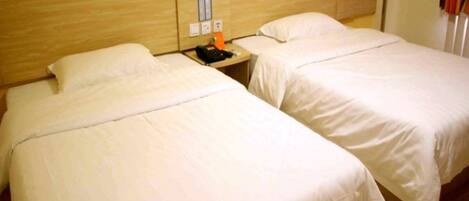 Two single beds with wooden headboards, a nightstand with a phone and a small table, and a wall-mounted light switch.