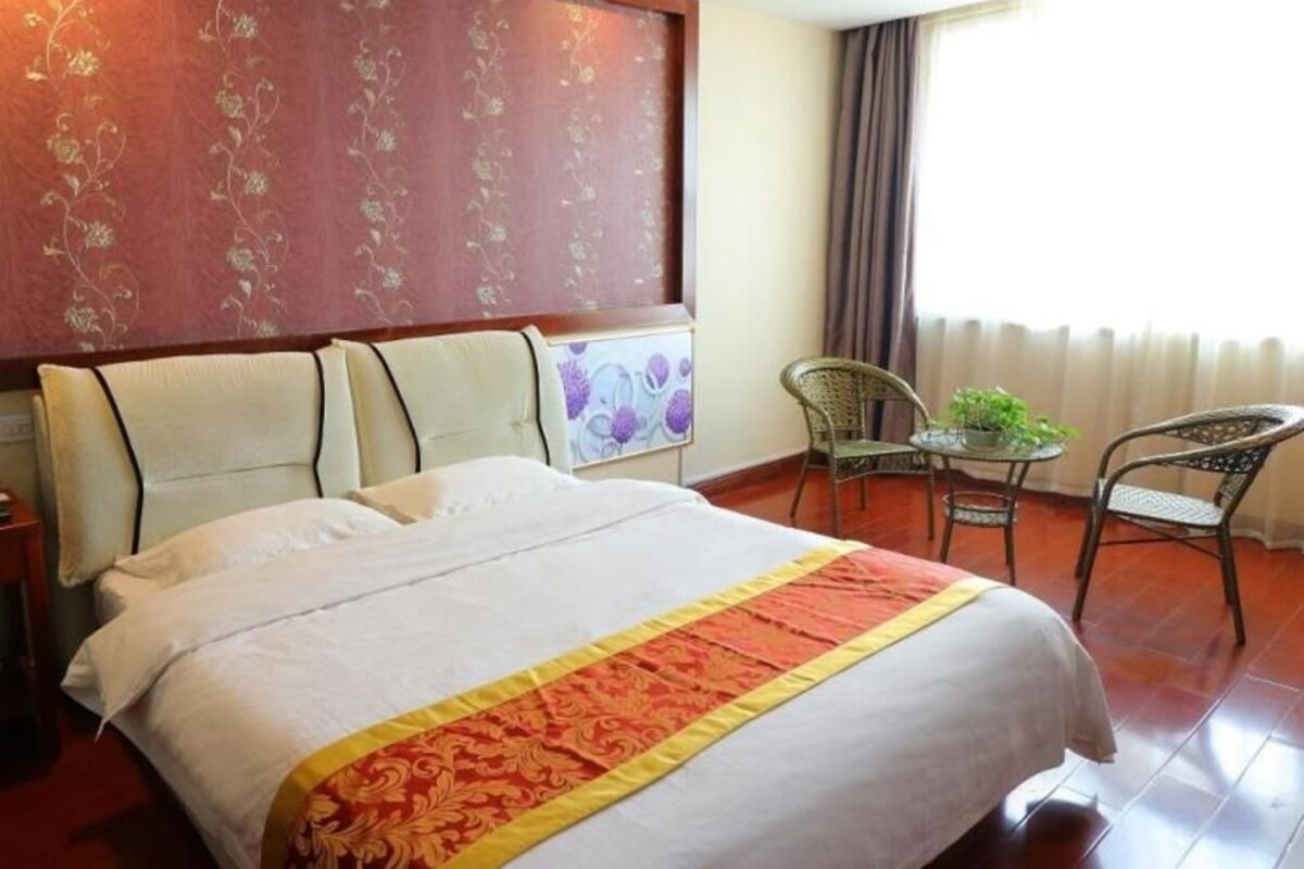 A hotel room with a large bed, a small table with chairs, and a window with curtains.