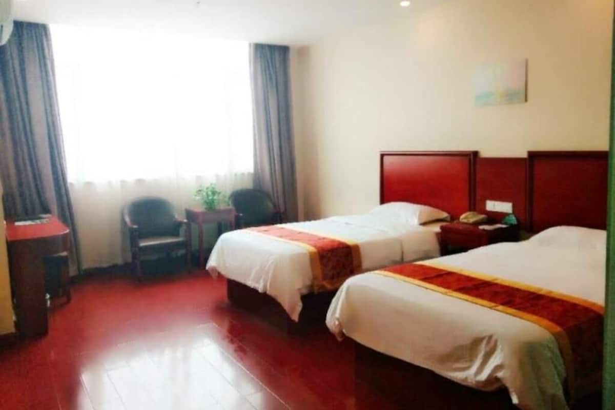A hotel room with two beds, a desk, a chair, and a window with curtains.