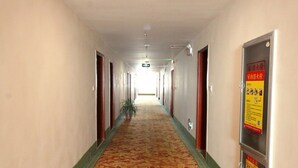 A hotel corridor with a carpeted floor, doors on both sides, and a sign on the right wall.