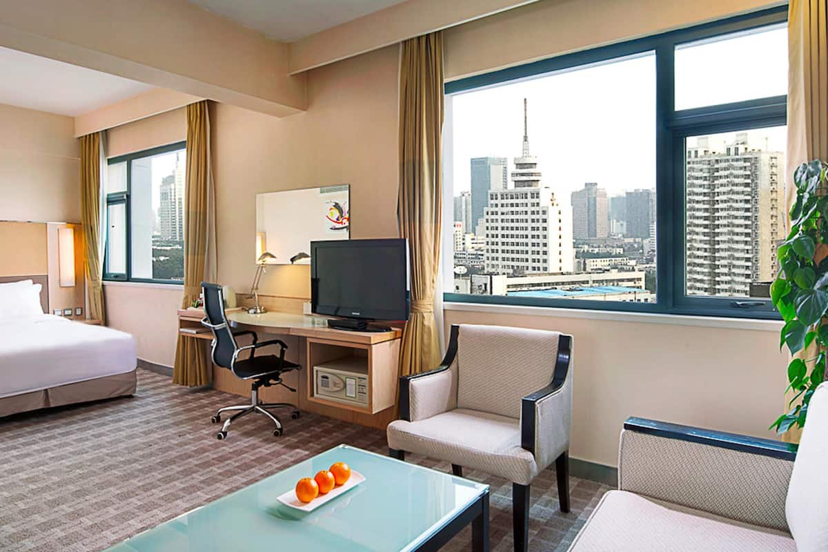 Habitación de hotel con cama, escritorio, silla, televisor y vista a la ciudad.