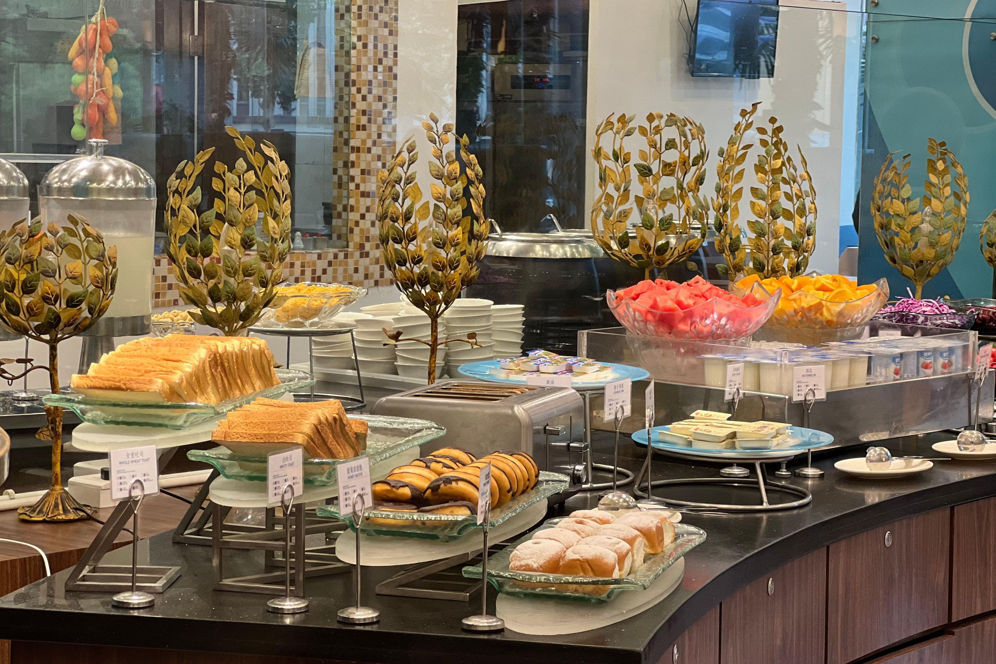 A buffet with various food items, including sandwiches, pastries, and fruits, displayed on glass trays with price tags.