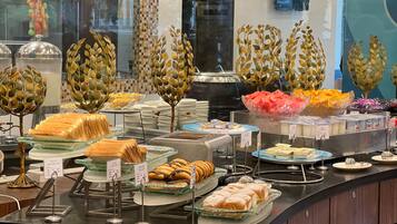 A buffet with various food items, including sandwiches, pastries, and fruits, displayed on glass trays with price tags.