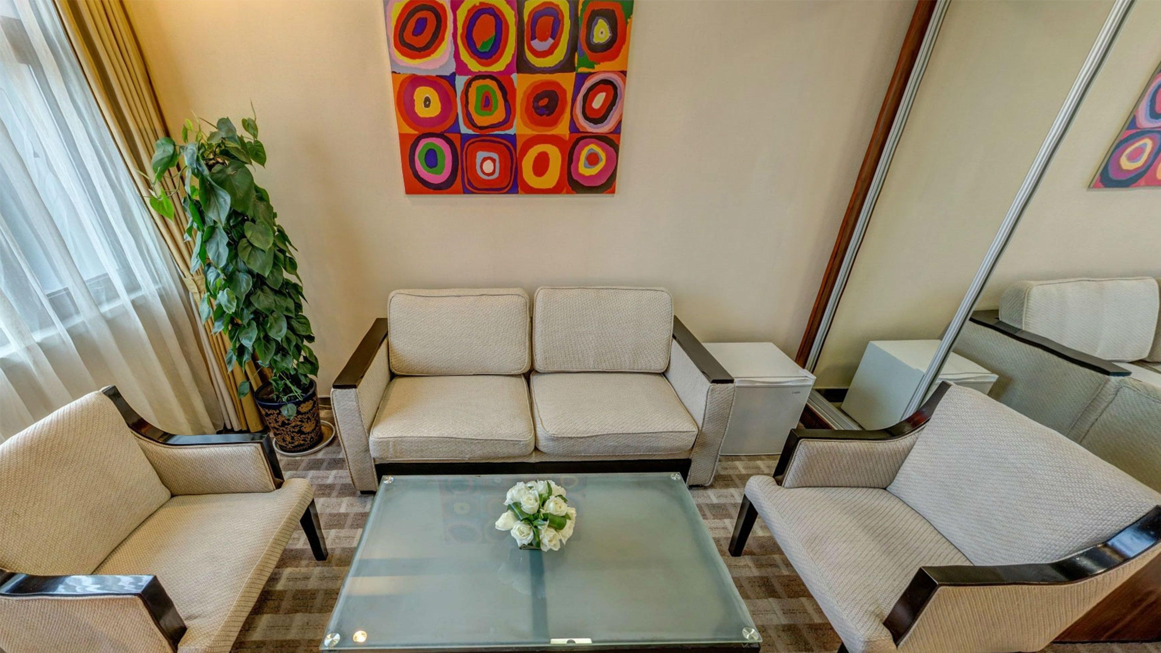 A modern living room with a sofa set, a coffee table with a floral centerpiece, and a colorful abstract painting on the wall.
