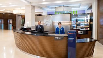 A reception desk with two staff members, a sign for the IHG Rewards Club, and a display of hotel amenities.