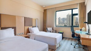 A hotel room with two beds, a desk, a chair, a lamp, and a view of a cityscape through a large window. - Holiday Inn Express Zhengzhou Zhongzhou (Zhengzhou)