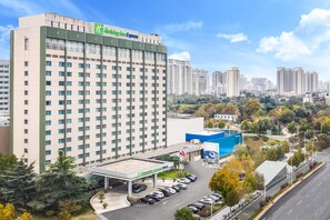 A hotel with a modern design, a parking area, and a view of the surrounding cityscape. - Holiday Inn Express Zhengzhou Zhongzhou (Zhengzhou)