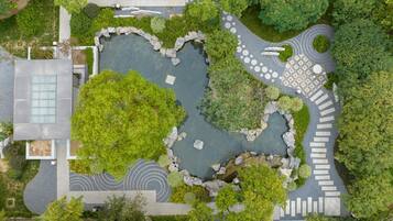 An aerial view of a landscaped area with a central pond, stone pathways, and surrounding greenery.