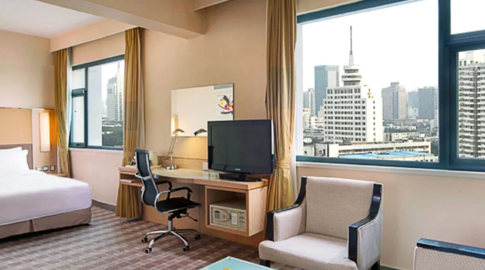 Quarto de hotel com cama, escrivaninha, cadeira, televisão e vista para a cidade.