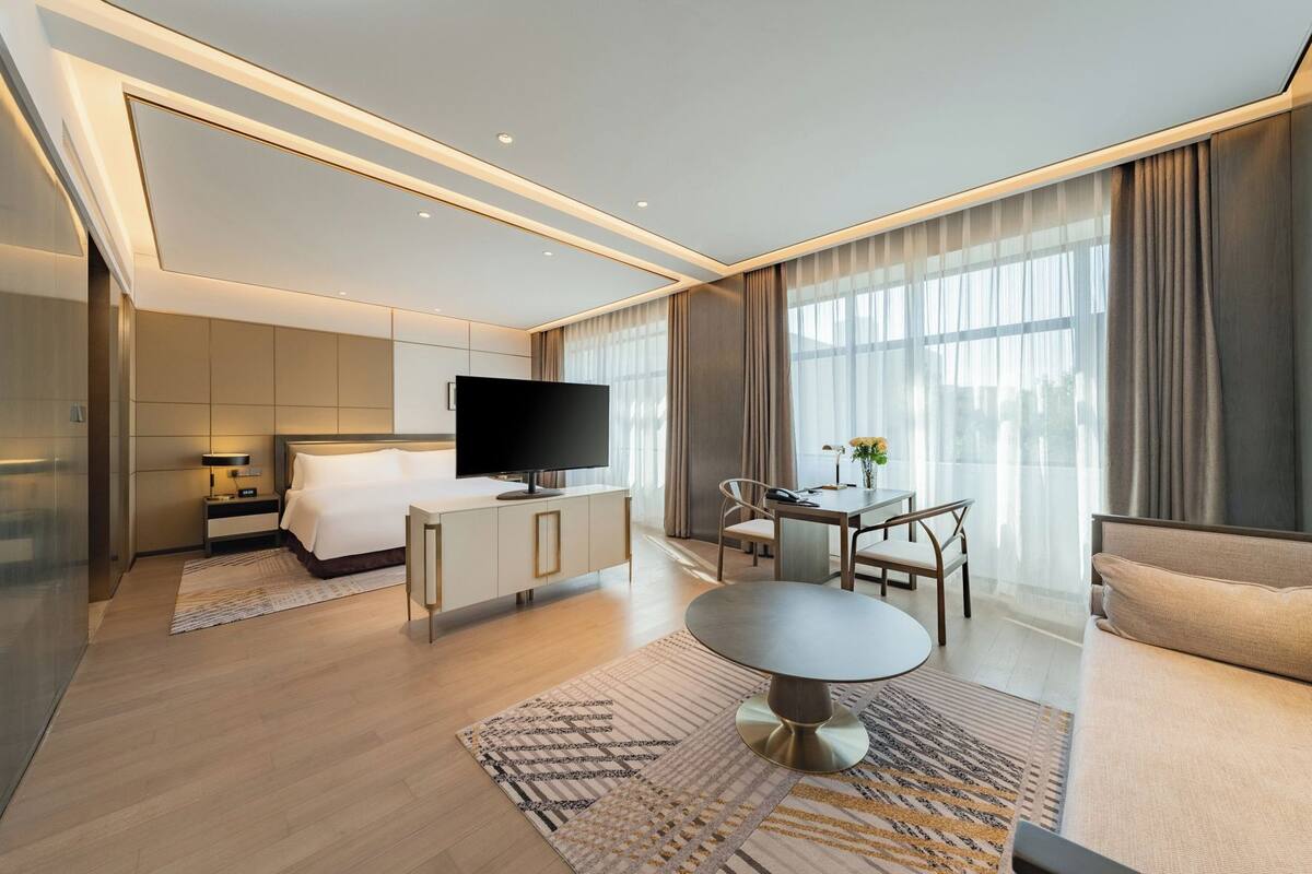 A modern hotel room with a bed, TV, dining table, and seating area.