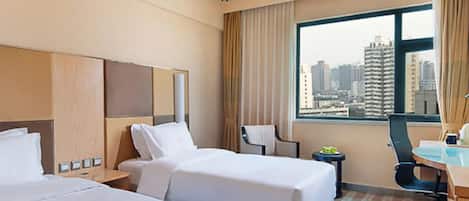 Habitación de hotel con dos camas, un escritorio, una silla, una mesita con frutas y vistas a un paisaje urbano a través de ventanas amplias.