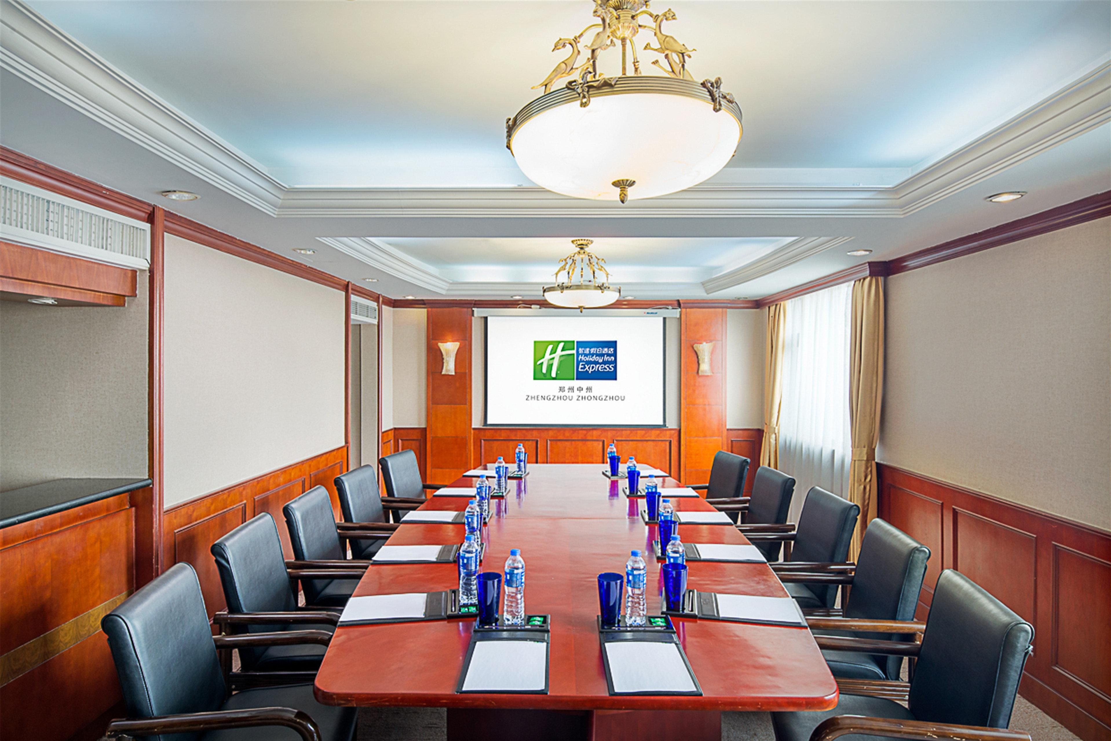A conference room with a long table, chairs, a projector screen, and a chandelier.