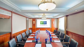 A conference room with a long table, chairs, a projector screen, and a chandelier.